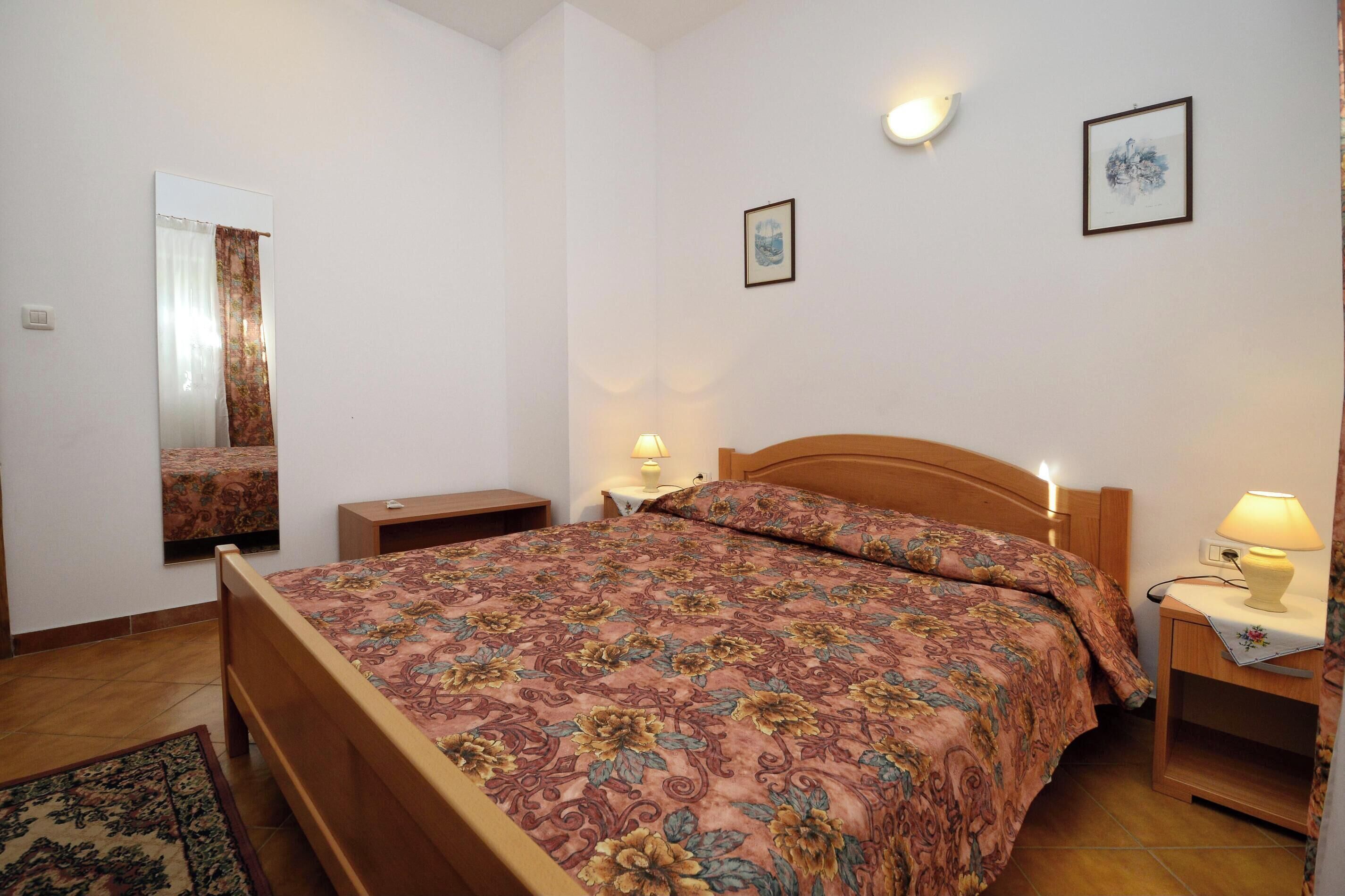 Una camera da letto con un letto in legno, un comodino con una lampada, uno specchio e un quadro appeso alla parete.