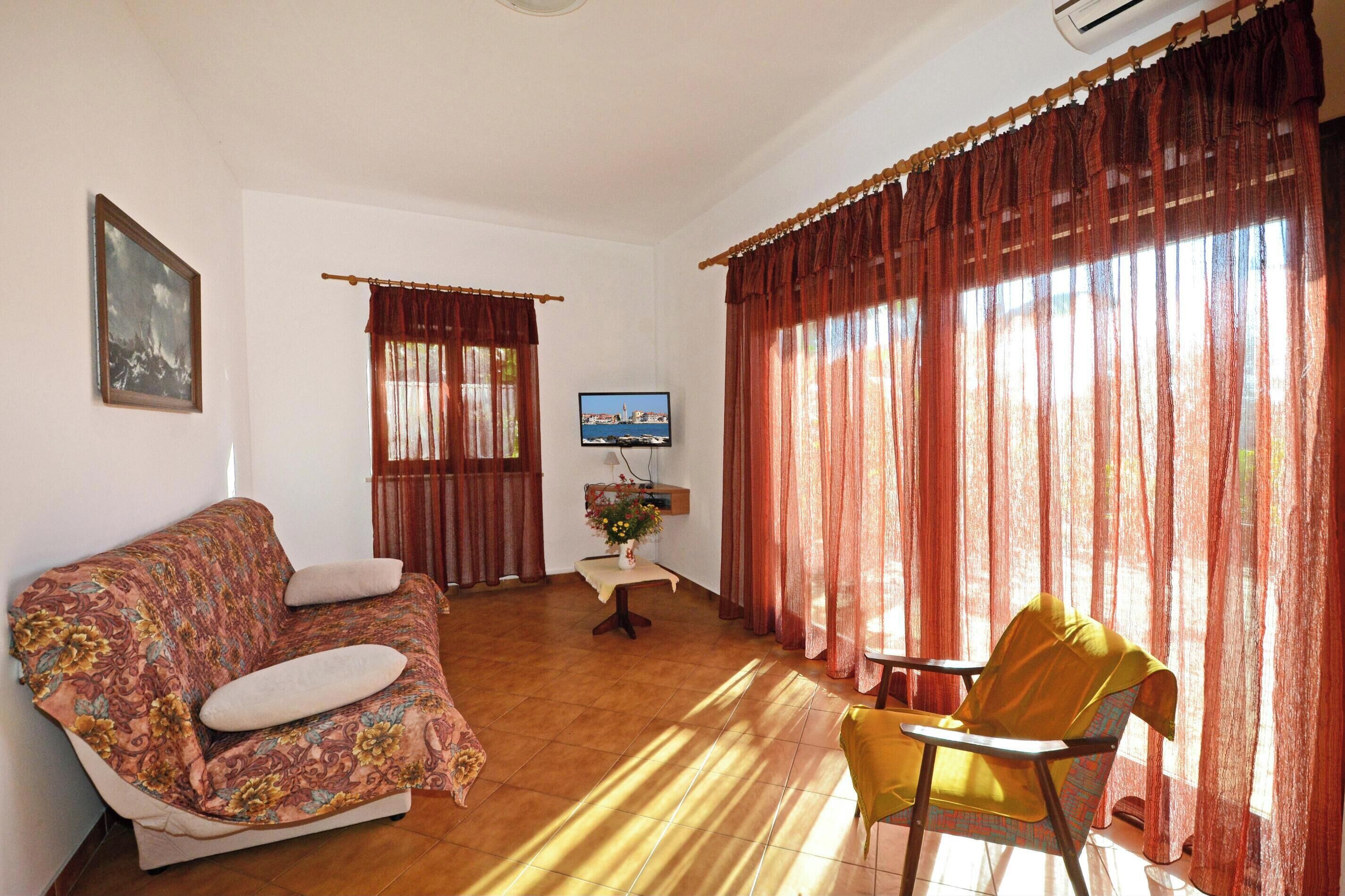 Una sala de estar con un sofá, una silla, un televisor y una mesa con un jarrón.
