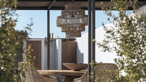 An outdoor dining area with wicker chairs and a wooden table, under a pergola with a hanging light fixture. - Bianco Boutique Villas - Eve (33F2+9P2 Pefki, Greece)