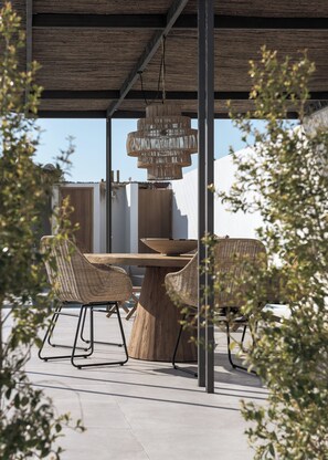 An outdoor dining area with wicker chairs and a wooden table, under a pergola with a hanging light fixture. - Bianco Boutique Villas - Eve (33F2+9P2 Pefki, Greece)