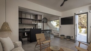 A modern living room with a sofa, two wicker chairs, a coffee table, and a kitchen area with a staircase leading to an outdoor area. - Bianco Boutique Villas - Eve (33F2+9P2 Pefki, Greece)