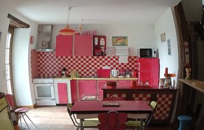 A kitchen with red and white checkered walls, a stove, microwave, and a dining area with chairs and a table. - Aux souvenirs d'Antan (Broyes)