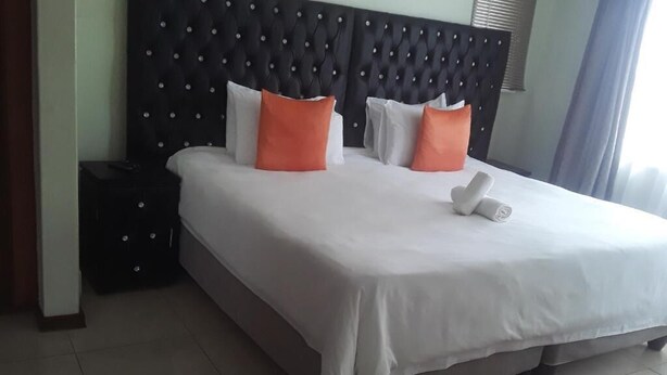 Una cama bien hecha con almohadas blancas y naranjas, un cabecero tapizado negro y una mesita de noche con una lámpara.