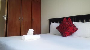 Una habitación de hotel con una cama, un armario de madera y un cojín rojo estampado.