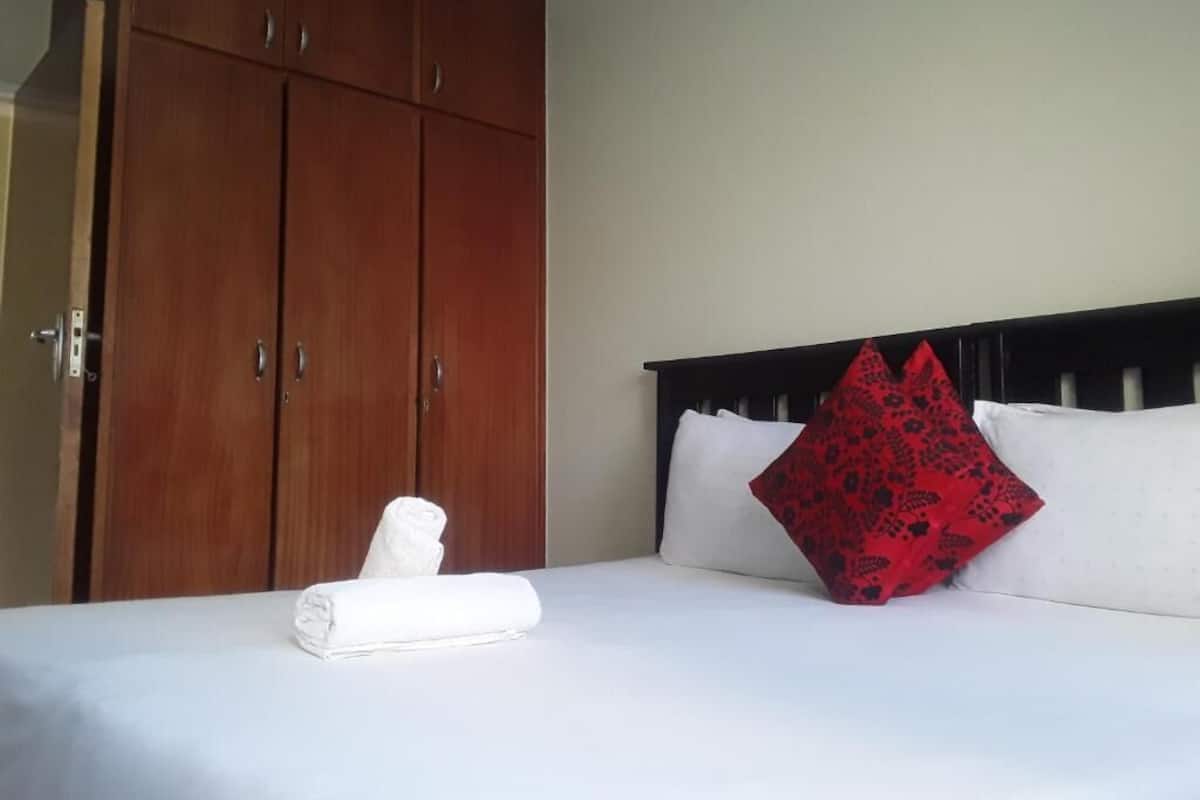Habitació d'hotel amb un llit, un armari de fusta i un coixí vermell estampat.