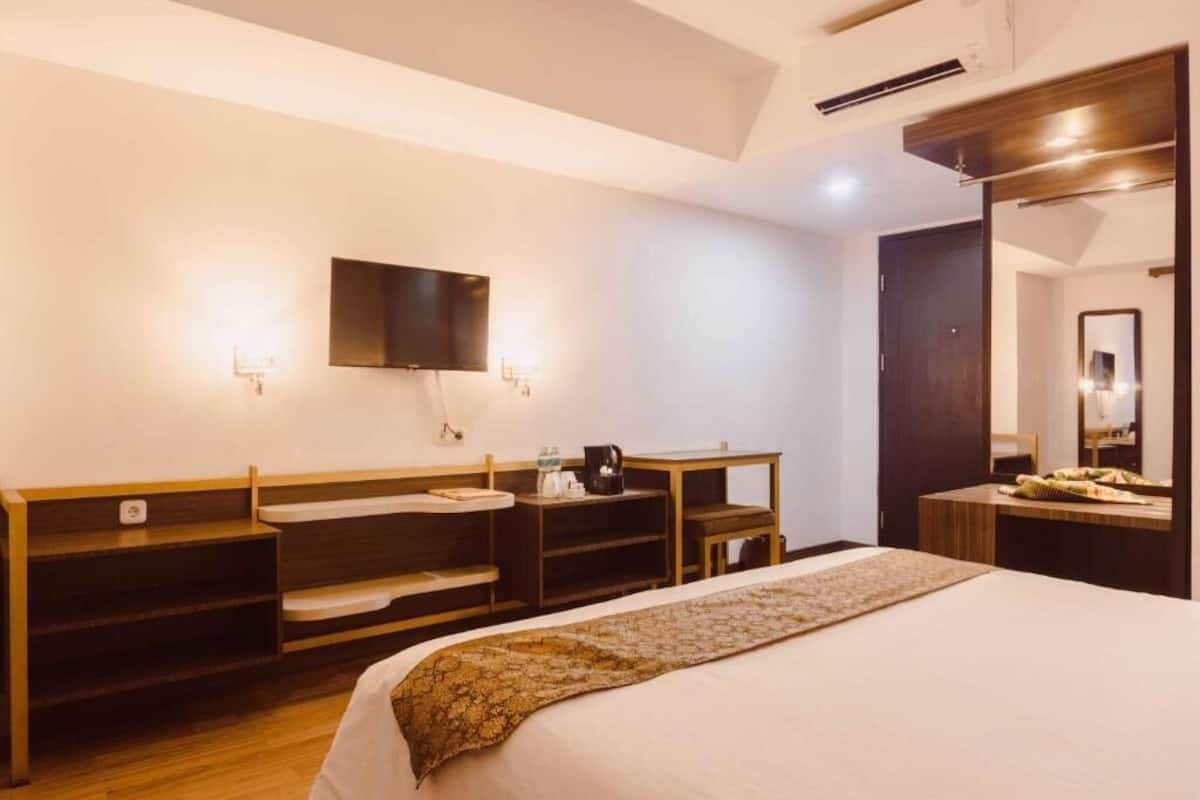 A hotel room with a bed, a desk, a chair, a mirror, and a television.