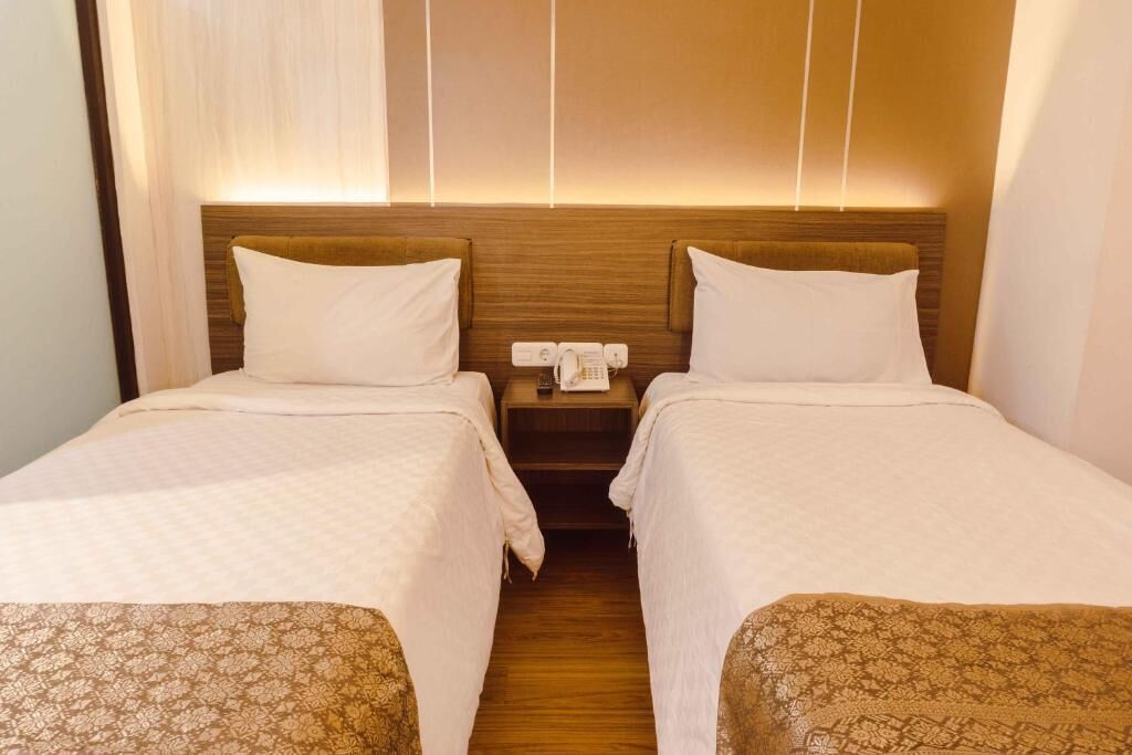 A hotel room with two beds, a wooden headboard, a bedside telephone, and a nightstand.
