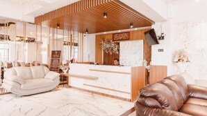 A hotel reception area with a wooden reception desk, a white sofa, and a brown leather sofa. - Fahira Hotel Bukittinggi Syariah (Bukittinggi)