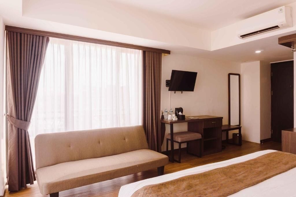 A hotel room with a sofa, a desk with a chair, a flat-screen TV, and a bed.