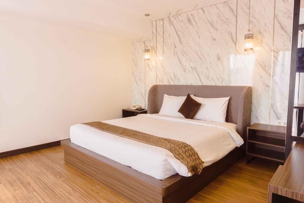 Camera d'albergo moderna con un letto grande, pavimento in legno, parete in marmo e comodino con lampada.