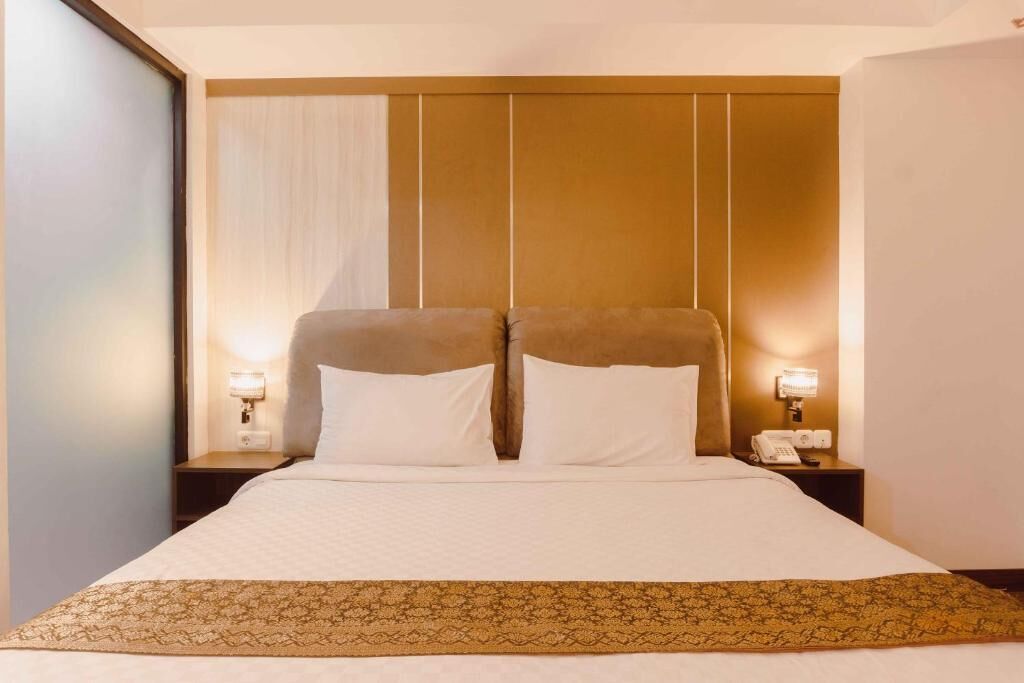 A hotel room with a large bed, two bedside tables, a telephone, and a wall-mounted light fixture.
