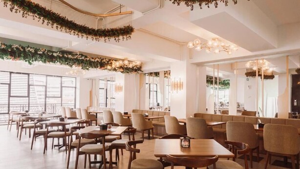 A modern restaurant interior with wooden tables and chairs, large windows, and decorative greenery on the ceiling. - Fahira Hotel Bukittinggi Syariah (Bukittinggi)