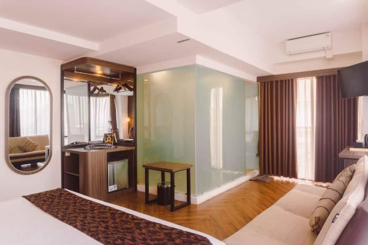 A modern hotel room with a wooden floor, a sofa, a small table, a mirror, and a television.