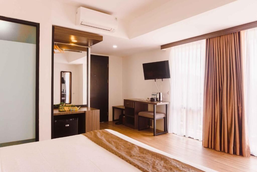 A hotel room with a bed, a desk, a chair, a TV, and a window with curtains.
