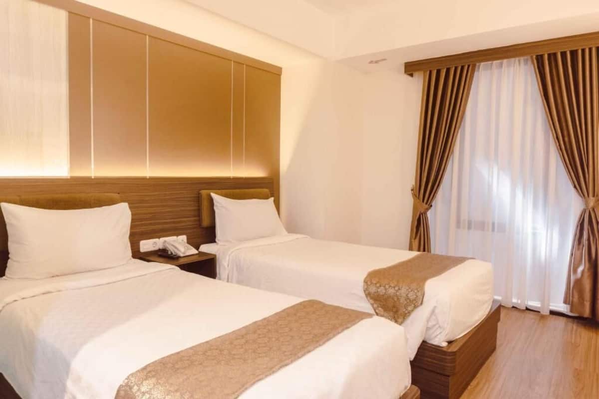A hotel room with two beds, a wooden headboard, a telephone, and a window with curtains.