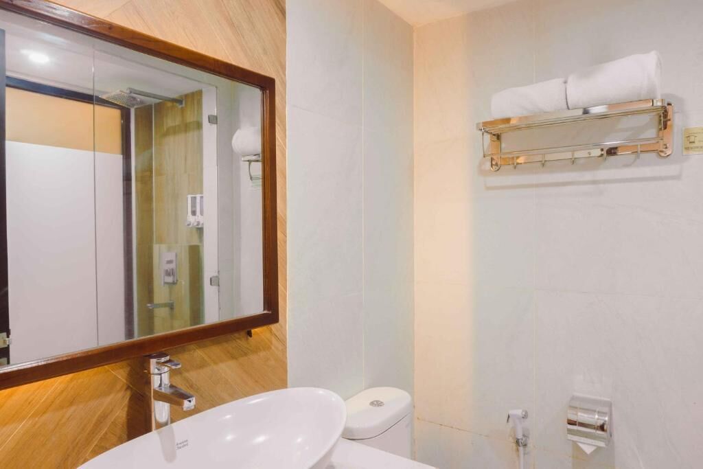 A modern bathroom with a large mirror, a white sink, a toilet, and a towel rack.
