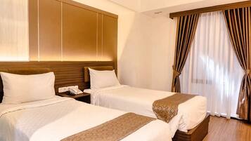 A hotel room with two beds, a wooden headboard, a bedside telephone, and a window with curtains.