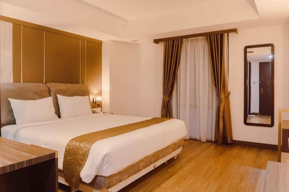 A hotel room with a large bed, wooden flooring, a mirror, and curtains.