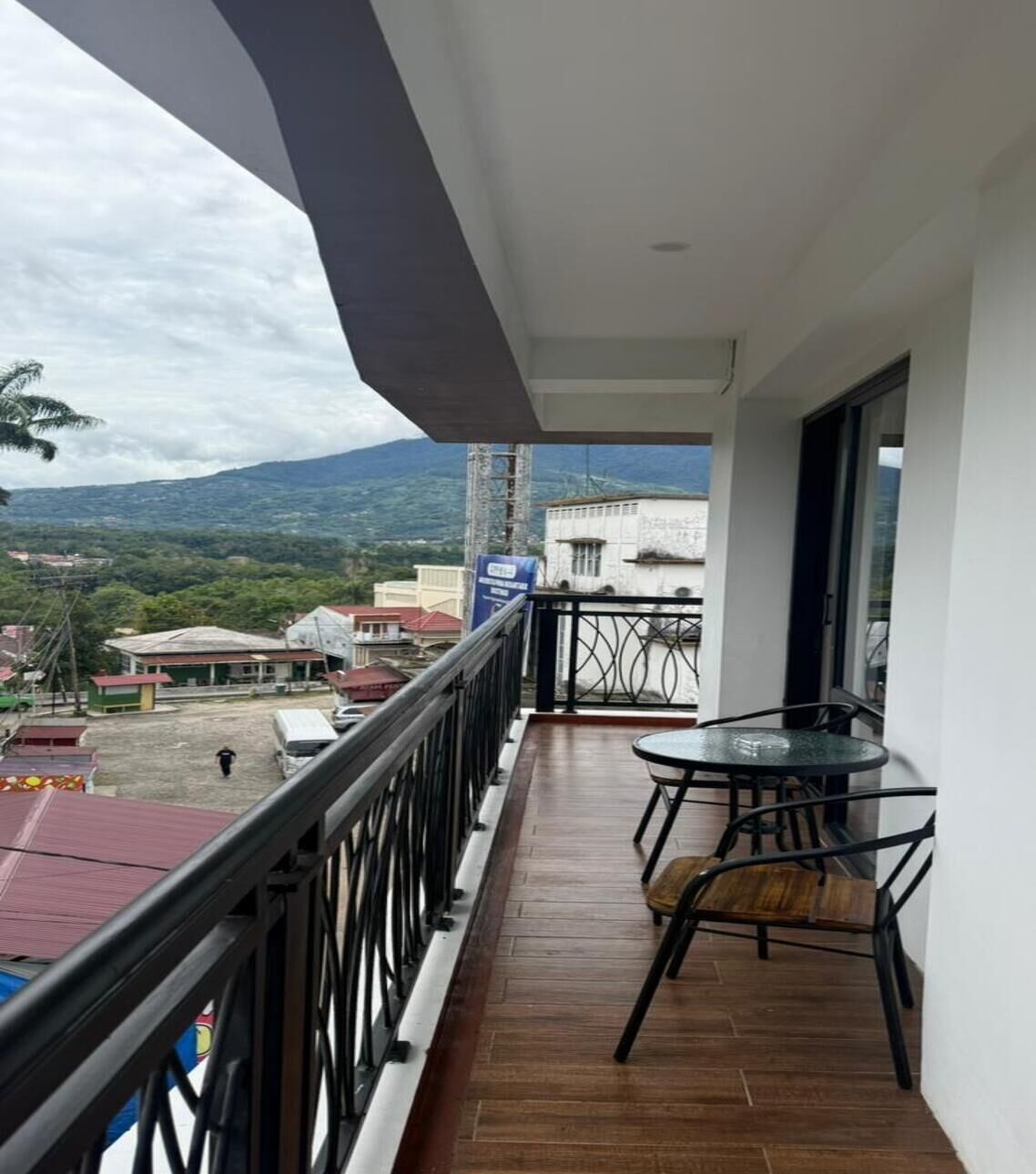 A balcony with a table and chairs, a view of a cityscape and mountains, and a signboard.