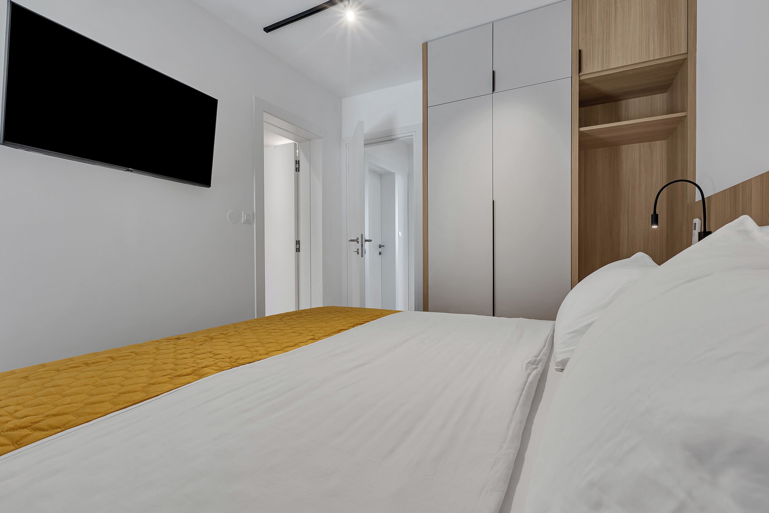 A modern bedroom with a bed, a wardrobe, and a TV mounted on the wall.