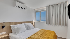 Een moderne hotelkamer met een bed, nachtkastje, airconditioning en een raam met gordijnen.