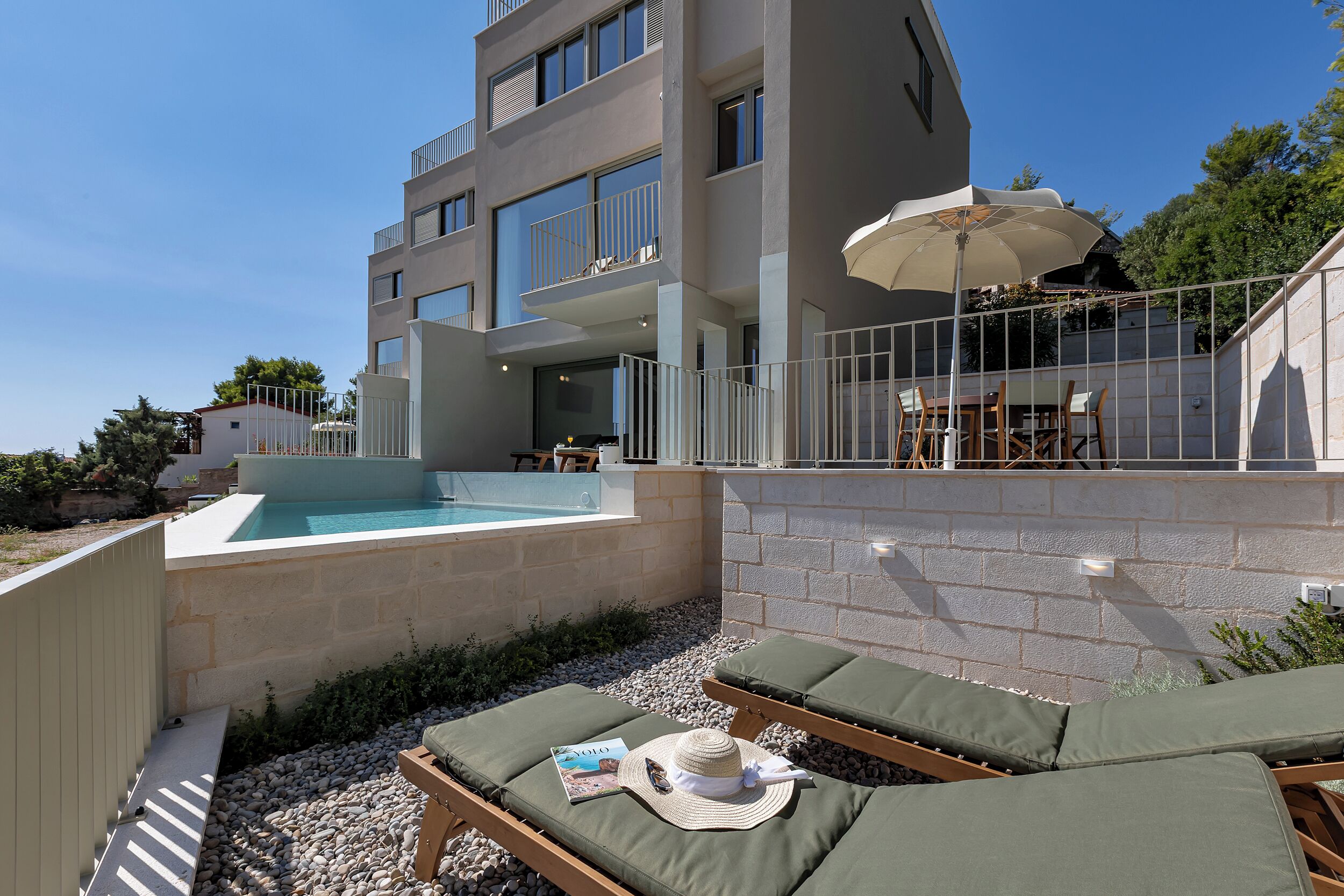 A modern building with a swimming pool, lounge chairs, and a patio area.