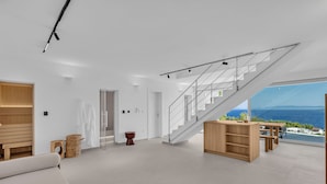 Een ruime woonruimte met een moderne trap, een houten bank en uitzicht op zee.