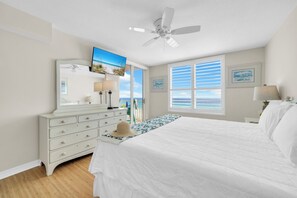 Ein Schlafzimmer mit Bett, Kommode, Deckenventilator, Fernseher und einem Fenster mit Jalousien.