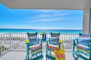 A balcony with two striped chairs, a small table with a plant and a bottle, and a beach view. - 🏖️Island Princess 501 Royal Lookout | Gulf Front+Pool | Beach Service🏖️ (Fort Walton Beach)
