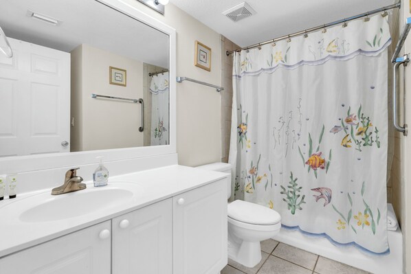 A bathroom with a white sink, a toilet, a shower curtain with a floral pattern, and a mirror above the sink. - 🏖️Island Princess 501 Royal Lookout | Gulf Front+Pool | Beach Service🏖️ (Fort Walton Beach)