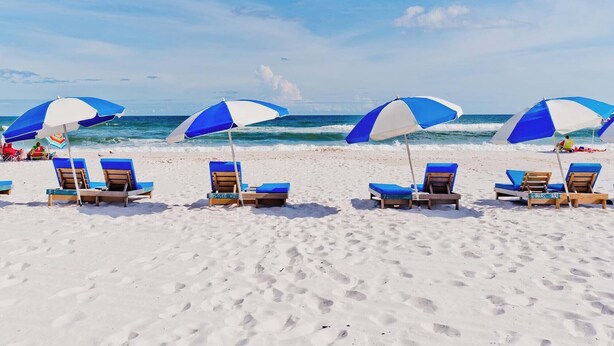 Una playa con hileras de sombrillas azules y blancas y sillas de playa.