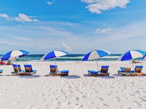 A beach with rows of blue and white beach umbrellas and lounge chairs. - Tradewinds #002 | Ground-Floor, Gulf-Front, Resort Pool + Snowbird-Friendly (Orange Beach)
