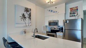 Una cocina moderna con armarios blancos, un refrigerador de acero inoxidable, un microondas y una estufa. Hay una isla grande con un fregadero y asientos tipo barra.