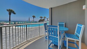 Un balcón con vistas a una piscina y una playa, con sillas y una mesa azules.