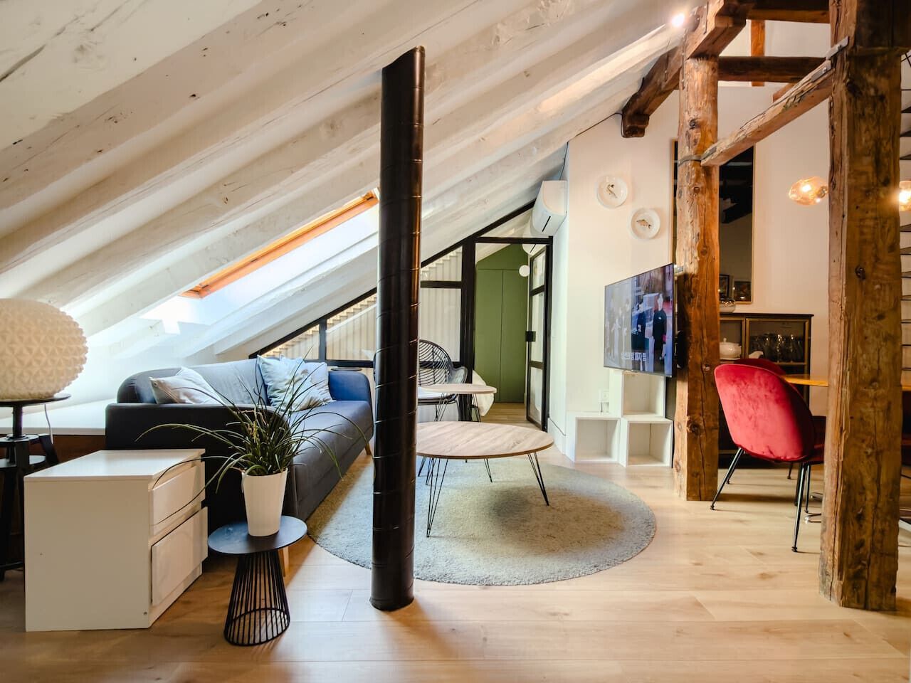 A loft-style room with a sloped ceiling, a sofa, a dining table, and a red chair.