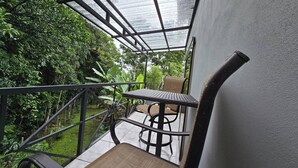 Een overdekt terras met een tafel en stoelen, omgeven door groen.
