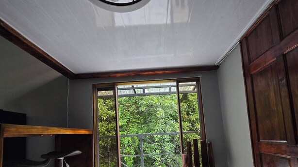 Een modern interieur met een plafondventilator, een bar met krukken en uitzicht op weelderige begroeiing door grote schuifdeuren.