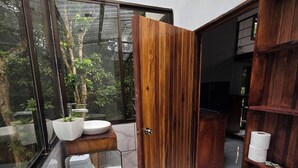 Een moderne badkamer met toilet, wastafel en douche, met een houten deur en marmeren tegels.