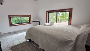 Een slaapkamer met een bed, twee ramen, een ventilator en een betegelde vloer.