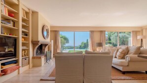 A spacious living room with a fireplace, a sofa set, and a large window offering a view of the outdoors. - Villa "Les Lucioles (Vence)