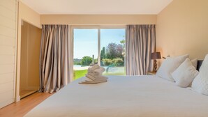 A hotel room with a large bed, a nightstand with a lamp, and a view of a garden through the window. - Villa "Les Lucioles (Vence)