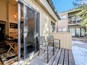 Une terrasse en bois avec deux chaises, une porte vitrée et une vue sur un immeuble à plusieurs étages.