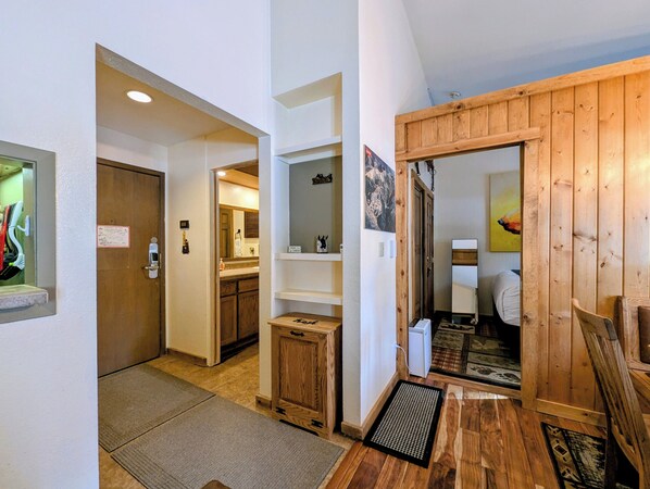 A hallway with wooden floors, a small wooden cabinet, a white door, and a mirror on the wall. - New Listing | King Beds | Pool/Hot tub (Keystone)