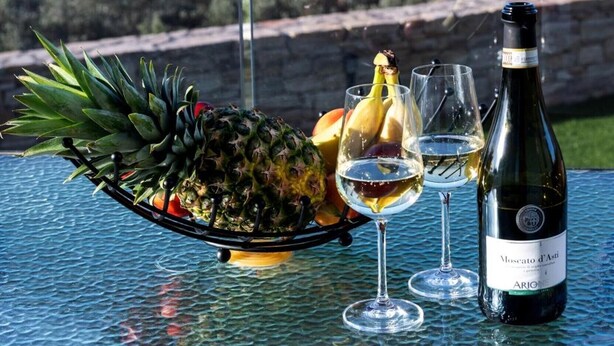 Una mesa con una botella de vino, dos copas y una presentación de frutas.