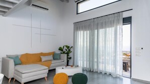 Una sala de estar moderna con sofá, otomanas, una mesa de centro y un amplio ventanal con cortinas.
