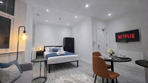 A modern hotel room with a bed, a desk, a chair, a TV, and a bathroom. - Luxury Studio Flat in Streatham | Close to Central London (London)