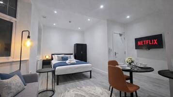 A modern hotel room with a bed, a desk, a chair, a TV, and a bathroom.