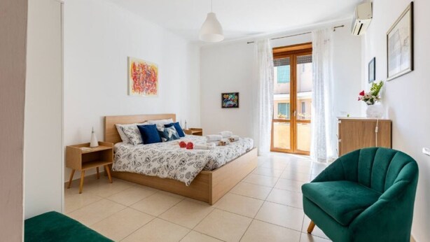A bedroom with a bed, bedside tables, a green armchair, and a window with curtains. - Wide and Bright, only a few steps from Colosseum & metro (Roma)