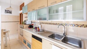 A modern kitchen with wooden cabinets, a double sink, and a tiled backsplash. - Wide and Bright, only a few steps from Colosseum & metro (Roma)