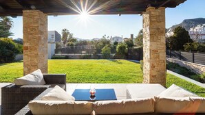 A covered outdoor seating area with stone pillars, a view of a grassy yard, and a mountain in the background. - Villa Amorata - Schinias Private Garden Retreat (Schinias)